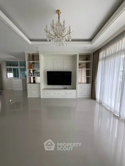 Elegant living room with chandelier and built-in TV unit, featuring large windows and natural light.