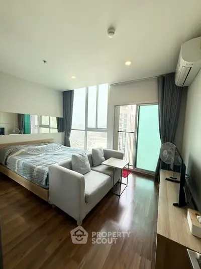 Modern bedroom with large windows and city view, featuring cozy seating and sleek design.