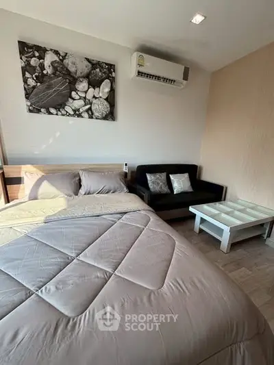 Cozy bedroom with modern decor and air conditioning, featuring a comfortable bed and stylish sofa.
