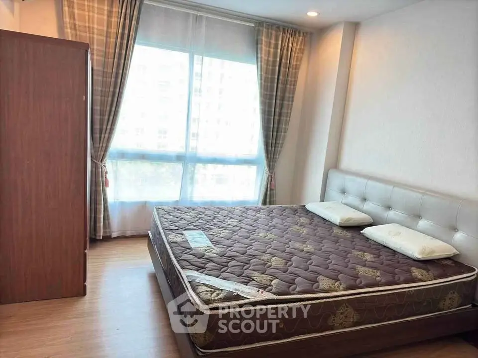 Spacious bedroom with large window and modern furnishings in a bright apartment.