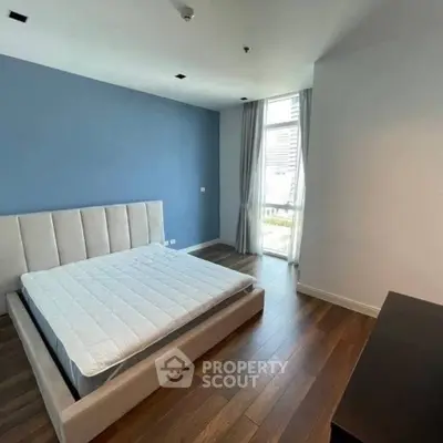 Modern bedroom with blue accent wall and large window in a stylish apartment.