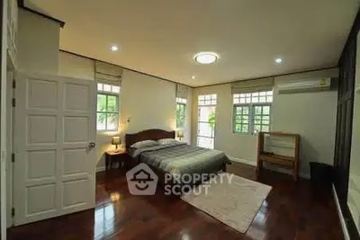 Spacious bedroom with wooden flooring and large windows for natural light.