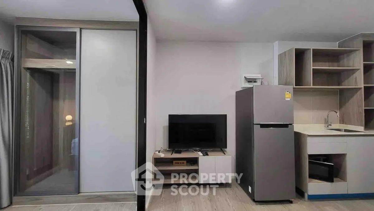 Modern apartment interior with sleek kitchen and living area featuring fridge and TV setup.