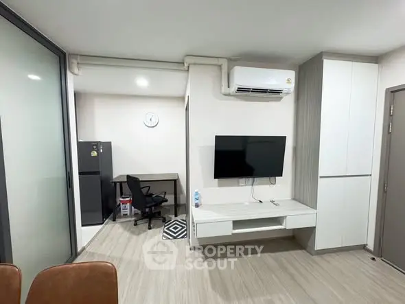 Modern living room with sleek design, featuring wall-mounted TV, air conditioning, and workspace with fridge.