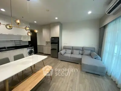 Modern living room with open kitchen, featuring sleek furniture and stylish lighting.