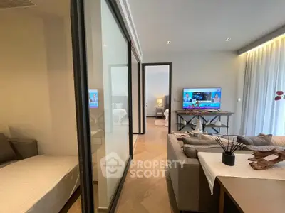 Modern living room with sleek design and natural light, featuring a cozy seating area and a flat-screen TV.