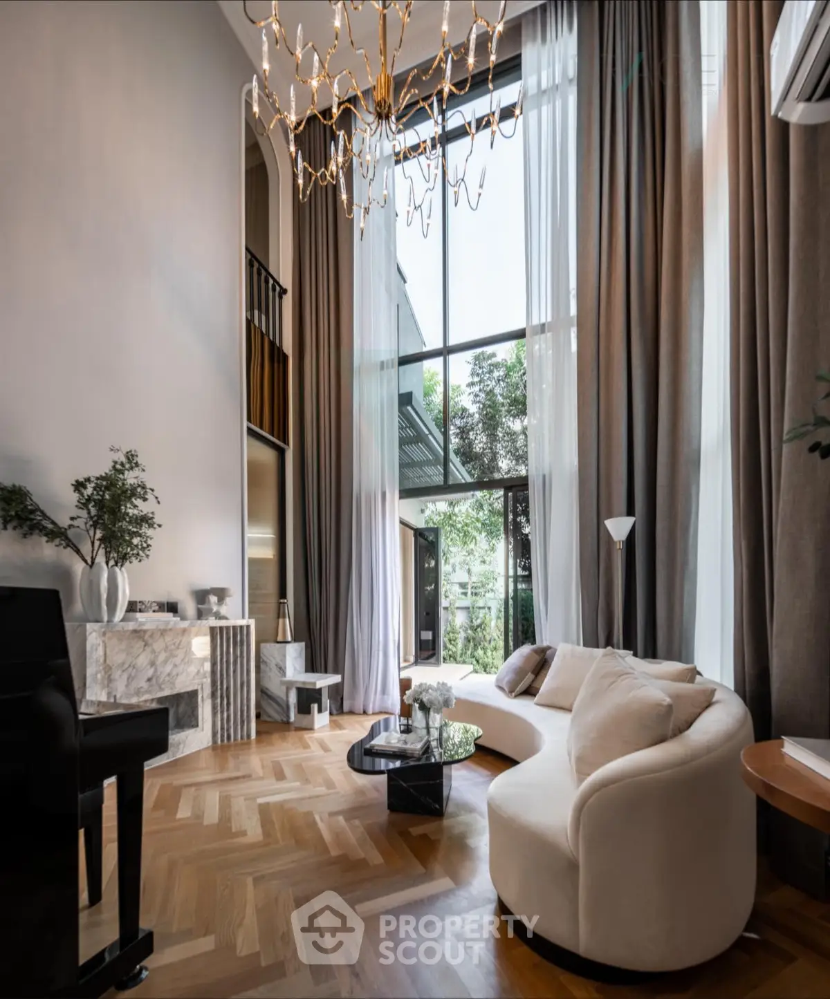 Luxurious living room with high ceilings, elegant chandelier, and floor-to-ceiling windows offering garden views.