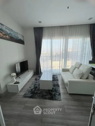 Modern living room with sleek white furniture and large windows offering natural light.