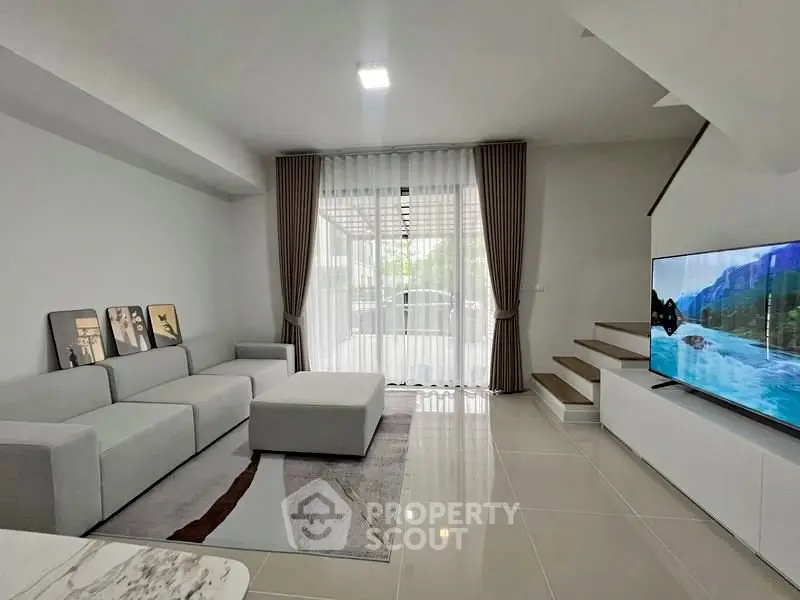 Modern living room with sleek design, large TV, and natural light from floor-to-ceiling windows.