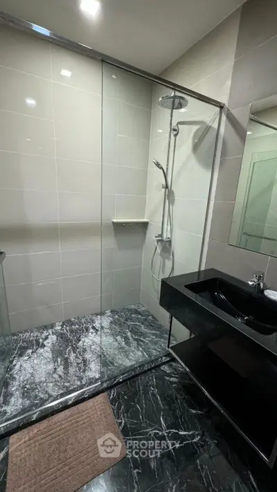 Modern bathroom with sleek black marble flooring and glass shower enclosure.