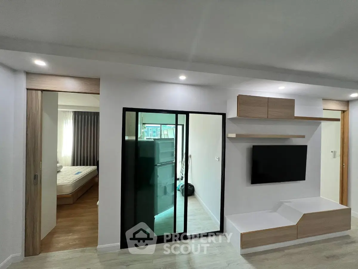 Modern apartment interior with sleek living room and bedroom view, featuring minimalist design and built-in TV unit.