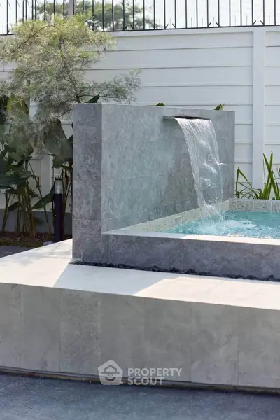 Luxurious outdoor pool with modern waterfall feature and elegant stone design, perfect for relaxation and entertainment.