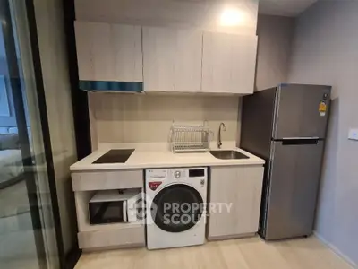 Modern compact kitchen with washing machine, microwave, and fridge in sleek apartment.