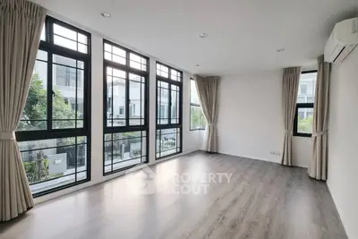 Spacious modern living room with large windows and elegant curtains, offering abundant natural light and a serene view.