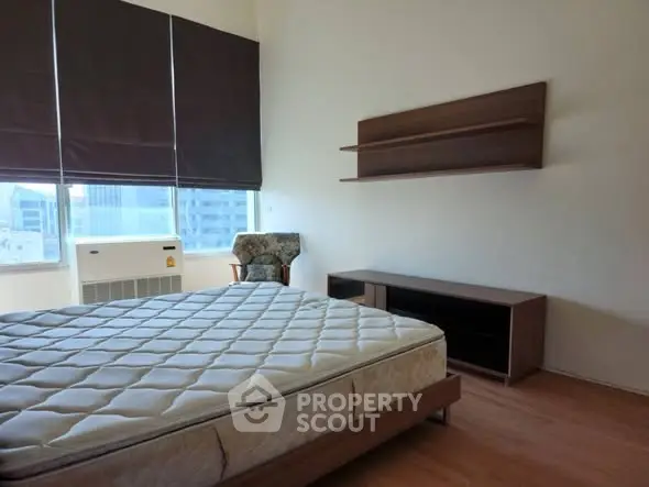 Spacious bedroom with large windows and modern furniture in urban apartment.