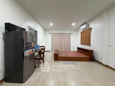 Spacious living room with modern decor and air conditioning, featuring a sleek refrigerator and cozy seating area.