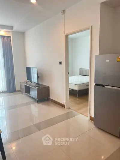 Modern apartment interior with sleek living room and visible bedroom, featuring stylish furniture and natural light.