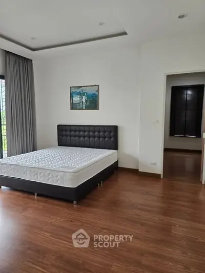 Spacious bedroom with wooden flooring and large window for natural light.