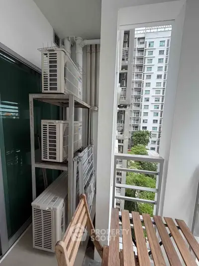 Modern apartment balcony with air conditioning units and outdoor seating, offering a view of neighboring buildings.