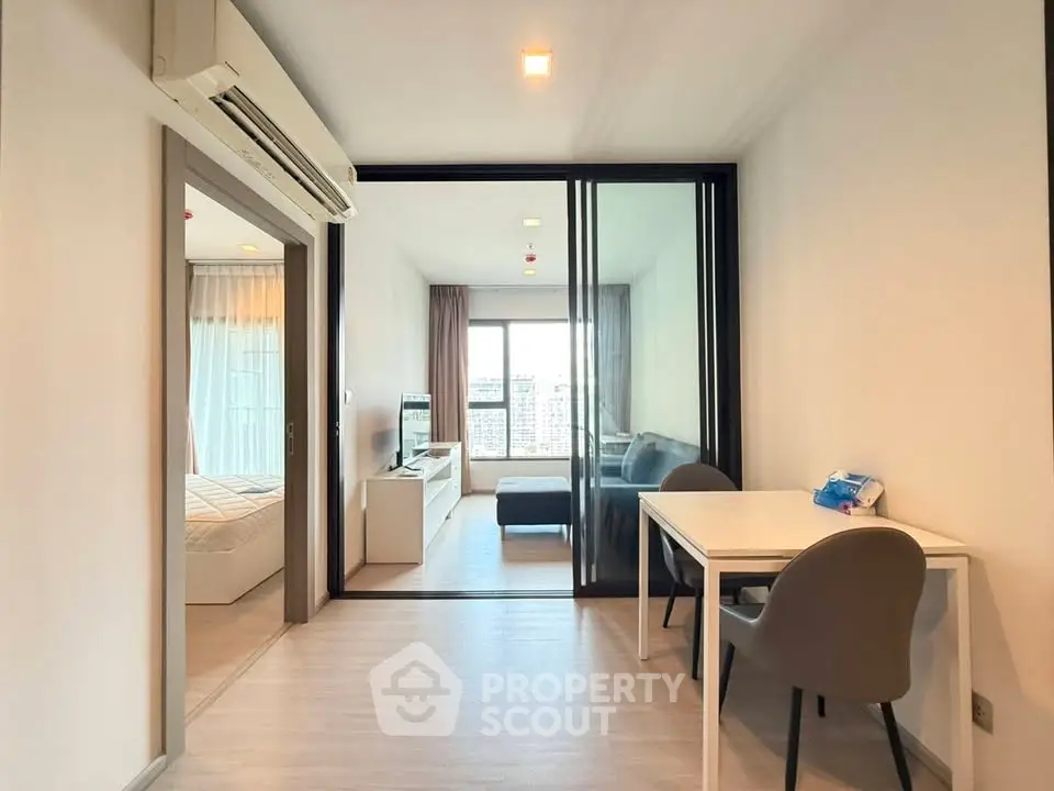 Modern apartment interior with open living area and bedroom, featuring sleek furniture and large windows.