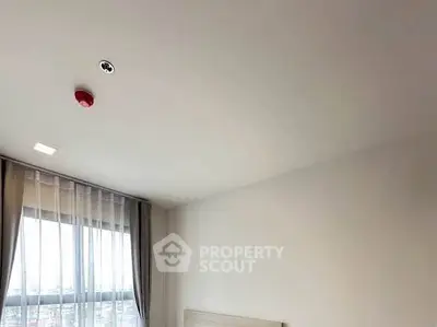 Modern bedroom with large window and ceiling fire alarm in a high-rise apartment.