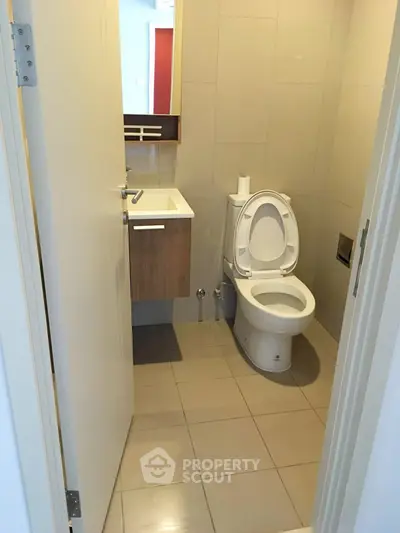 Modern bathroom with sleek fixtures and neutral tiles, featuring a compact vanity and toilet.