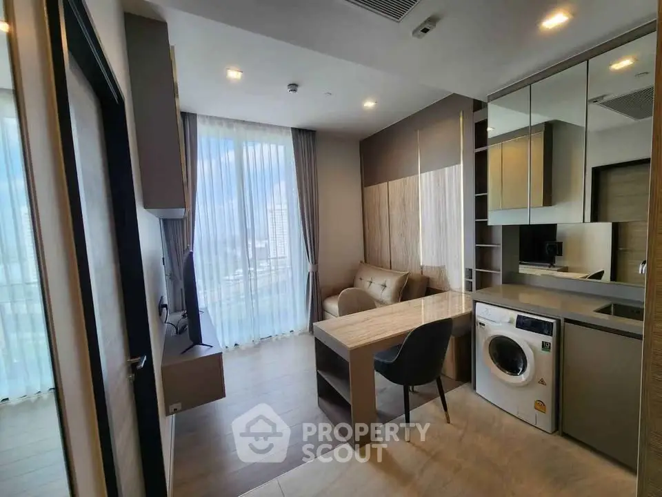 Modern living room with integrated kitchen and washing machine, featuring floor-to-ceiling windows and stylish decor.