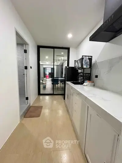 Modern kitchen with sleek white cabinetry and open layout leading to a stylish living area.