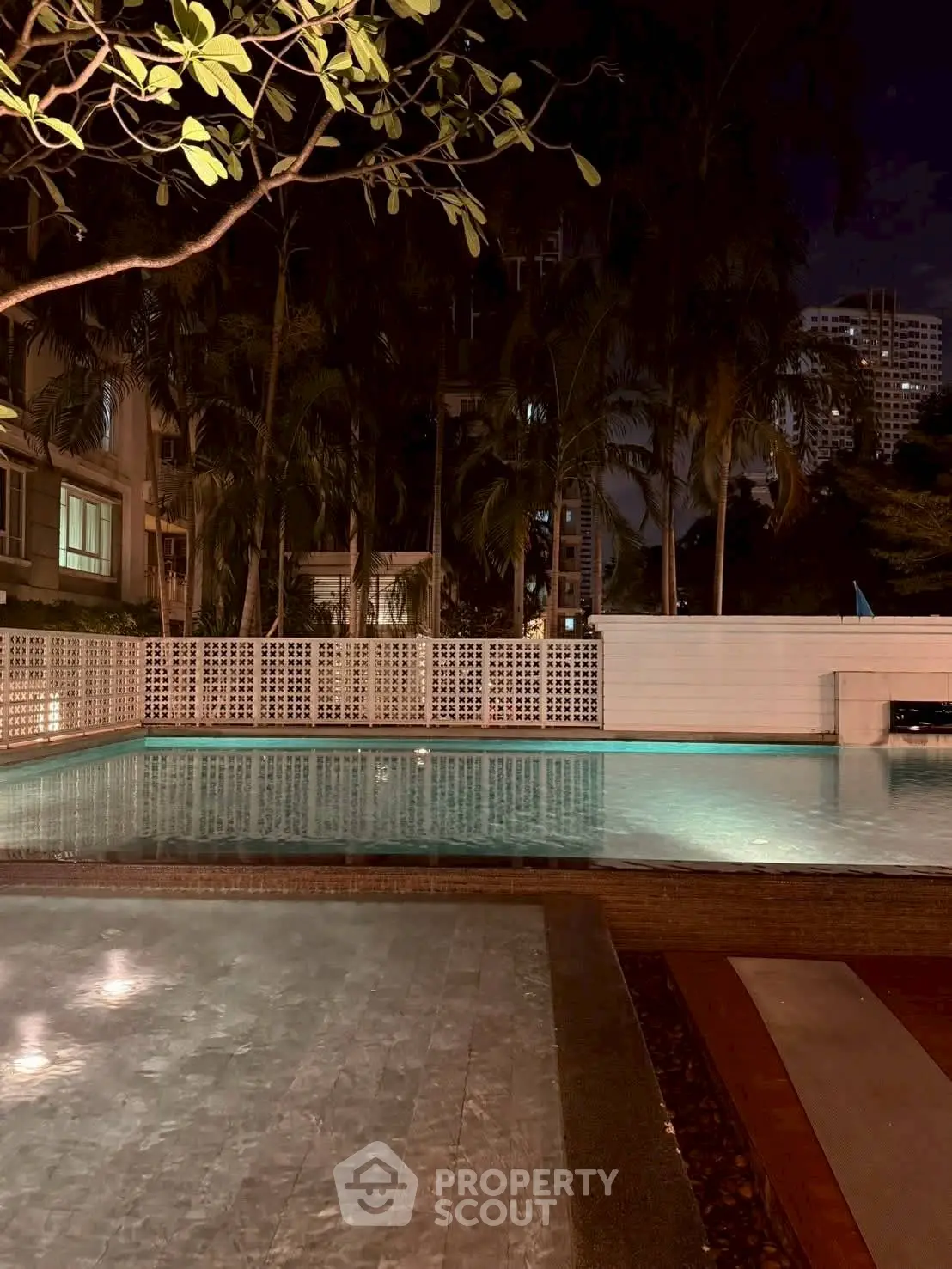 Luxurious night view of a serene residential pool surrounded by lush greenery and modern architecture.
