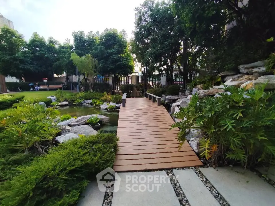 Tranquil garden with wooden bridge and lush greenery in serene real estate setting.