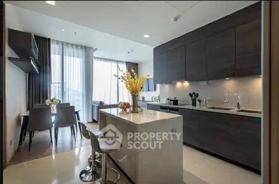 Modern open-layout kitchen with island and dining area, featuring sleek cabinetry and large windows.