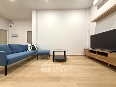 Modern living room with blue sofa, wooden flooring, and sleek TV stand.