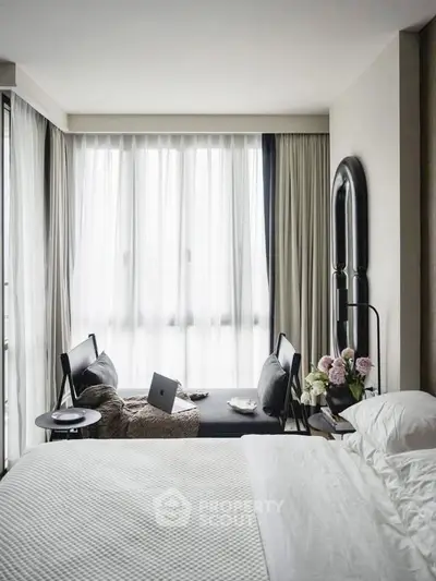 Modern bedroom with large window, cozy seating area, and elegant decor.