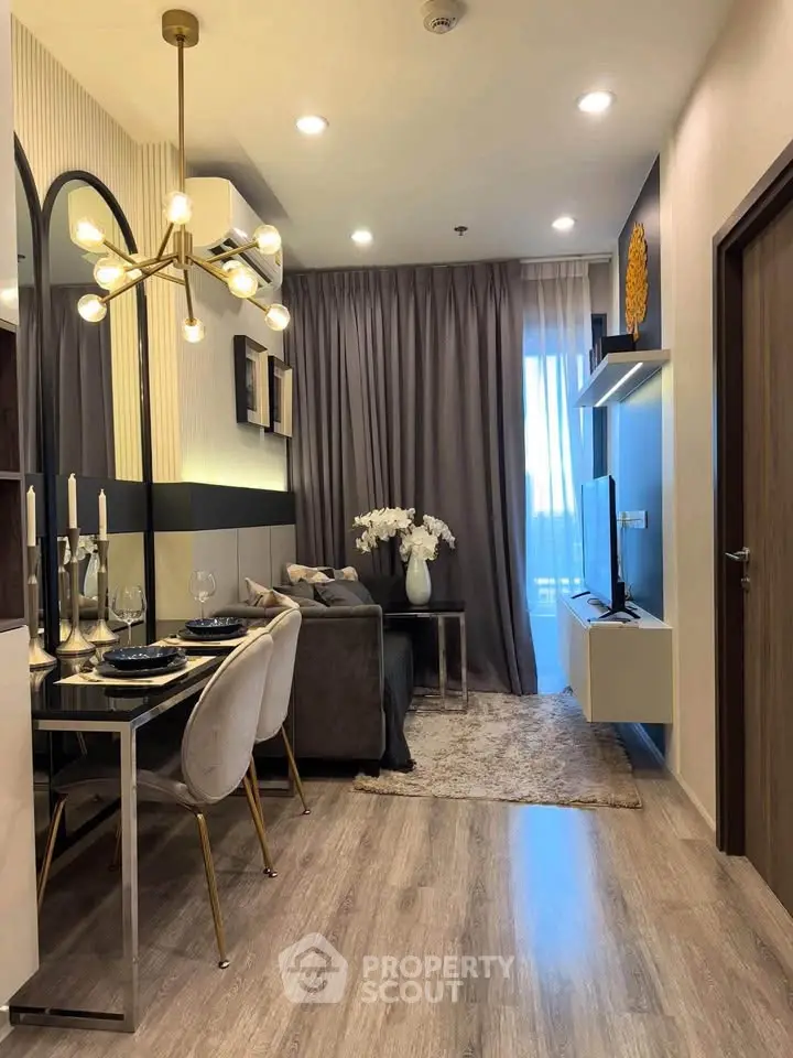 Modern living room with elegant decor, featuring a stylish chandelier, cozy seating, and a sleek TV setup.