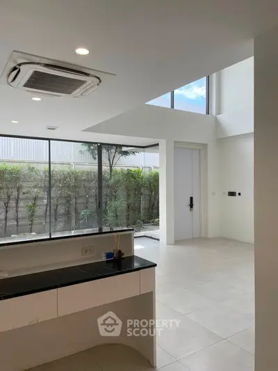 Modern open-plan living area with large windows and garden view, featuring sleek design and abundant natural light.
