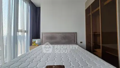 Spacious bedroom with large window and modern furnishings in a high-rise apartment.