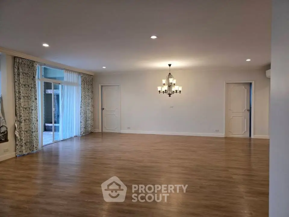 Spacious empty living room with elegant chandelier and large windows.