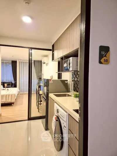 Modern apartment interior with kitchen and bedroom view, featuring sleek appliances and stylish decor.