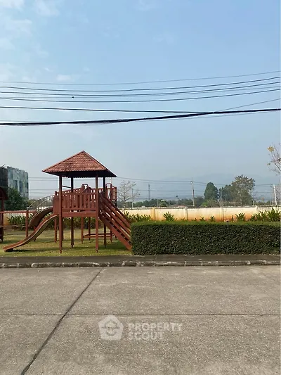 Charming outdoor playground area in a residential community with lush greenery and clear skies.