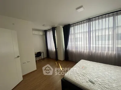 Spacious bedroom with large windows and natural light, featuring a modern design and air conditioning.