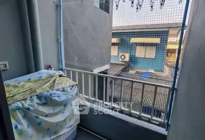 Cozy balcony with protective netting and covered washing machine, overlooking neighboring buildings.
