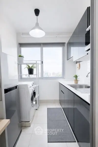 Modern kitchen with sleek cabinets and washing machine, featuring a bright window view.
