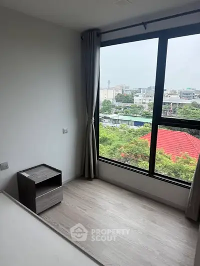 Bright bedroom with large window offering a stunning city view, perfect for urban living.