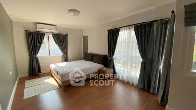 Spacious bedroom with large windows and elegant curtains, featuring a comfortable bed and wooden flooring.