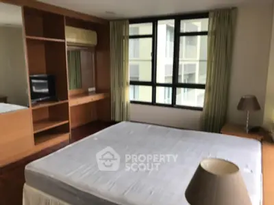 Spacious bedroom with large windows and built-in wooden wardrobe in modern apartment.