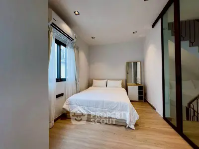 Modern bedroom with minimalist design, featuring a cozy bed, wooden flooring, and ample natural light.