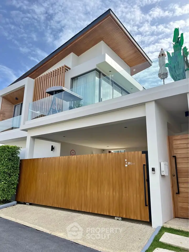 Modern two-story house with wooden accents and glass balcony under a clear blue sky.