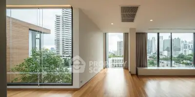 Spacious modern living room with large windows offering stunning city views, featuring sleek wooden flooring.