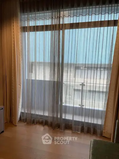 Spacious room with large window and sheer curtains offering natural light and urban view.