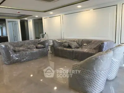 Spacious living room with elegant furniture wrapped for protection, showcasing modern design and glossy flooring.